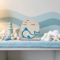 Personalized wood whale birth announcement sign on a nursery shelf with pastel blue ocean decor