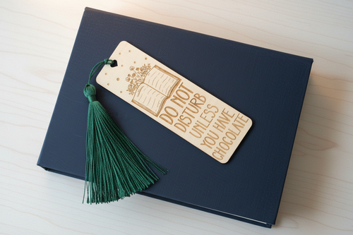 Do Not Disturb Unless You Have Chocolate laser engraved wood bookmark with dark green tassel flat lay on closed book cover