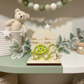 Personalized wood turtle birth announcement sign on a nursery shelf with pastel green decor